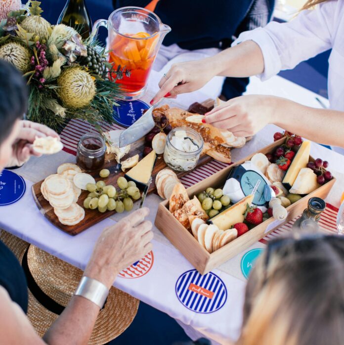 Crop people having picnic with drinks and food